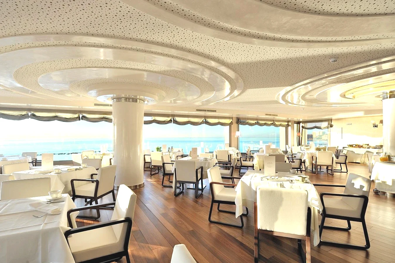 Restaurante con mesas y sillas blancas con vistas al mar en el Vincci Selección Aleysa Benalmádena